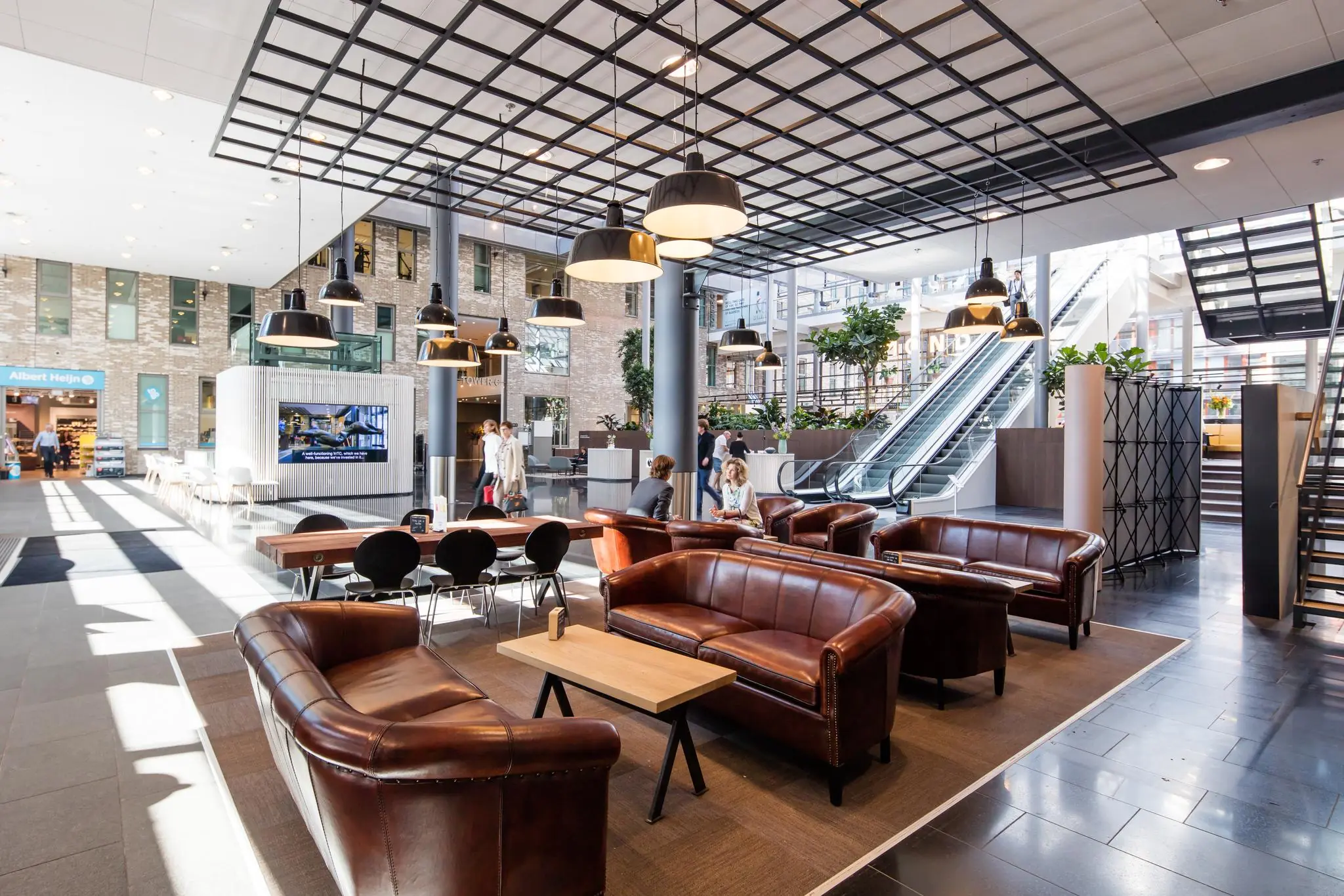 Moderne, lichte lobby aan de Prinses Beatrixlaan met leren zithoeken, een trap, roltrappen en een Albert Heijn-filiaal op de achtergrond.